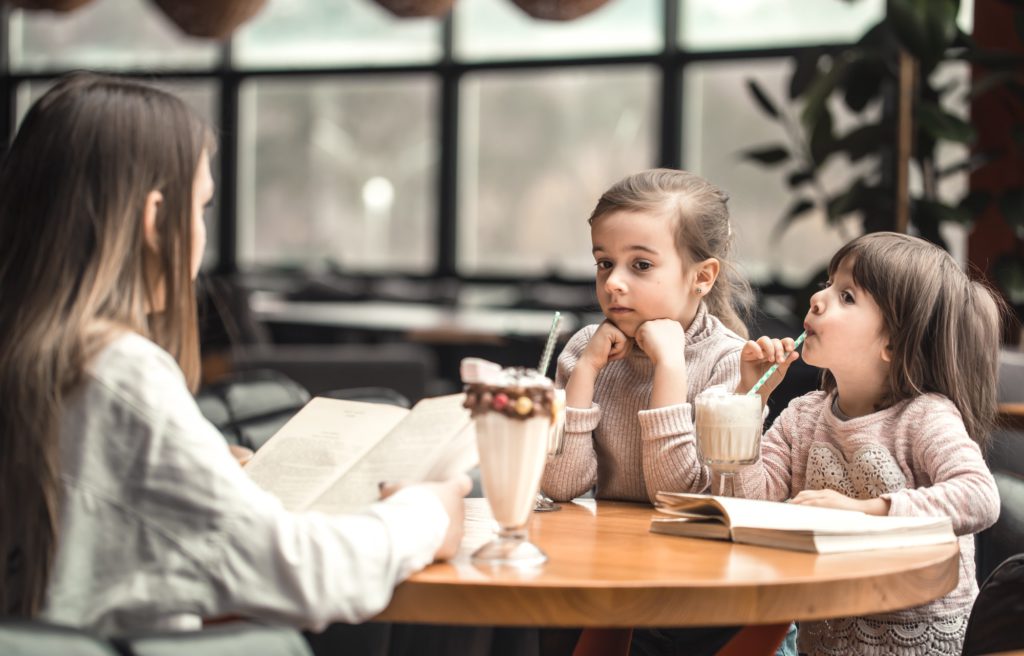 Happy young women mother with children sitting at dinner table and talking in restaurant