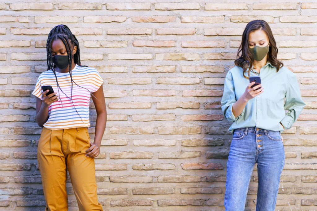 Multiethnic young women wearing masks using smartphone separated to respect social distance