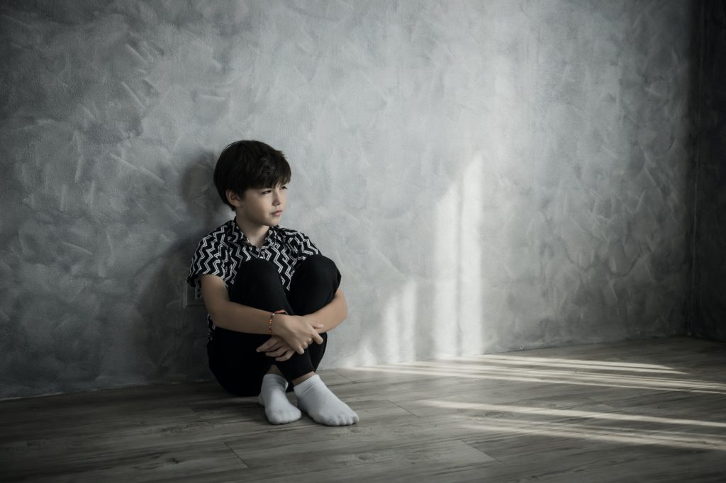 Sad boy sitting thinking sitting on the floor of the room against the house wall.